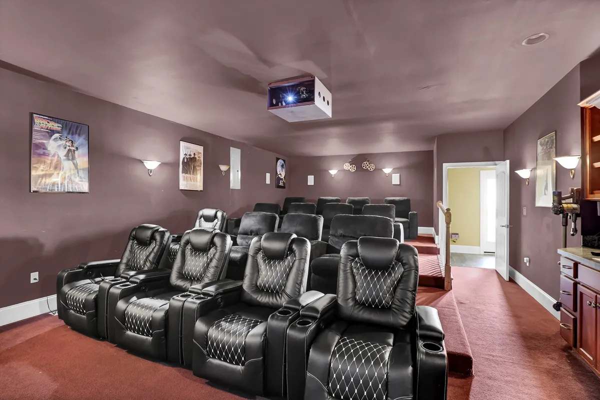 This image showcases a private movie theater featuring luxurious black leather recliner seats arranged for optimal viewing, a ceiling-mounted projector, and classic movie posters lining the walls. The lighting creates a cozy yet immersive atmosphere perfect for cinematic experiences.