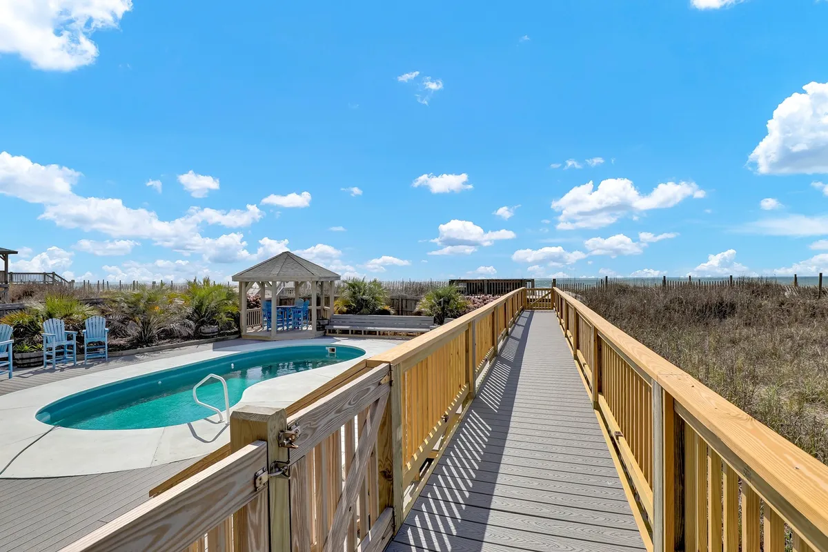 A tranquil pool area featuring a wooden walkway, picturesque gazebo, inviting swimming pool, and multiple lounge chairs. The setup is ideal for both daytime swims and evening stargazing, fitting perfectly with the section’s mention of enjoying the stars from the hot tub and poolside patio. The landscaping and layout suggest an environment tailor-made for group enjoyment and relaxation.