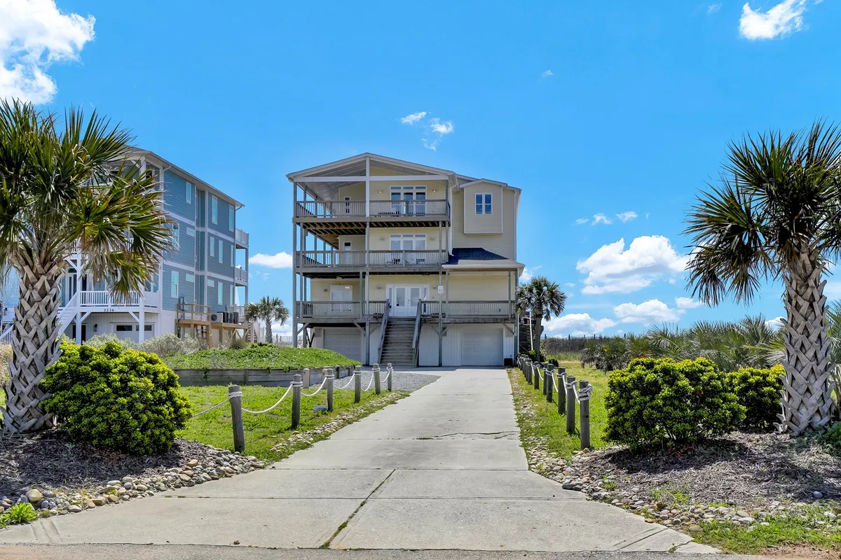 The main house framed by palm trees, a wide driveway, and well-manicured landscaping. The open design and spacious entryway create a welcoming first impression, with visible porches and pathways that suggest easy access to the entrance.