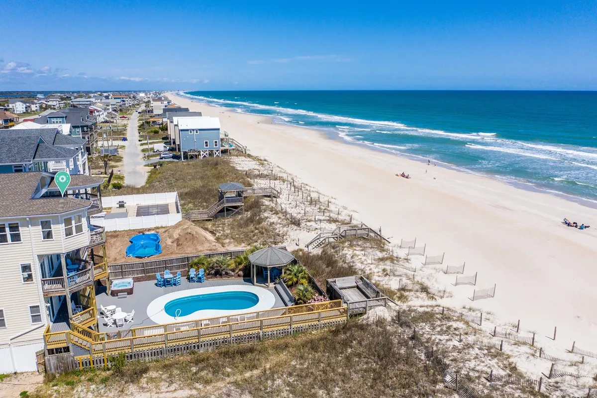An exterior scene featuring a sparkling swimming pool with a beachfront backdrop, a cozy gazebo, and surrounding homes. The setup is ideal for outdoor dining, family gatherings, and beach lounging, all with easy access to the ocean.