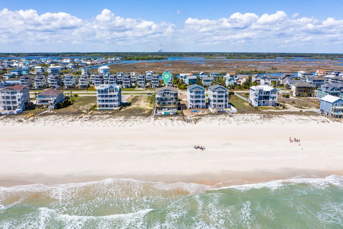 This image captures beachfront houses lining the sandy shore of North Topsail Beach with gentle ocean waves and people walking along the beach. The natural light and relaxed atmosphere highlight the proximity of homes to the beach, with clear visual access to the shoreline and recreational activity.