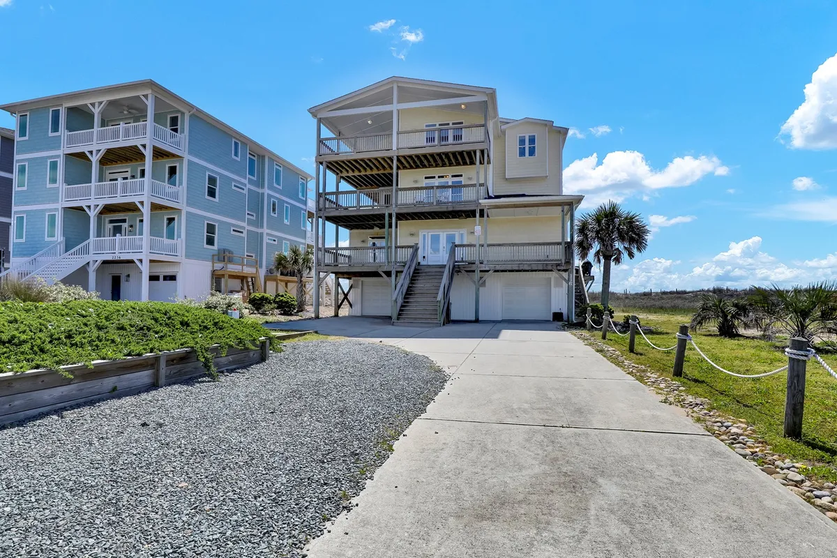 The exterior of the multi-level main house is surrounded by palm trees, with a driveway and inviting porch spaces. The home’s design suggests room for pets to explore and provides a welcoming first impression for families arriving with dogs.