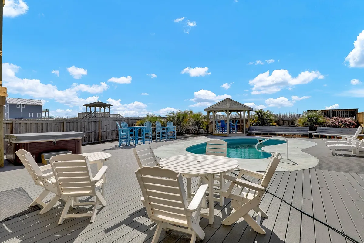 This image showcases a vibrant outdoor pool area featuring a spacious swimming pool, a relaxing hot tub, ample outdoor seating, a gazebo, and lush landscaping. The atmosphere is lively, with the space clearly designed for group gatherings, lounging, and unwinding. The setting beautifully captures both day and night poolside moments, highlighting the transition from sunbathing to cozy evenings in the hot tub.