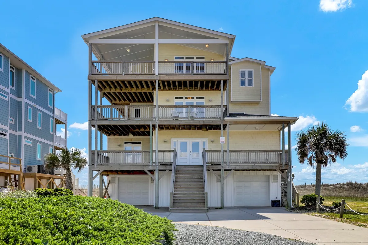 A three-story structure surrounded by lush greenery, with expansive balconies on each level and a large patio, alluding to multiple entry points and levels of the property. The image conveys a sense of scale and accessibility, hinting at the different ways guests might navigate or enter the house.