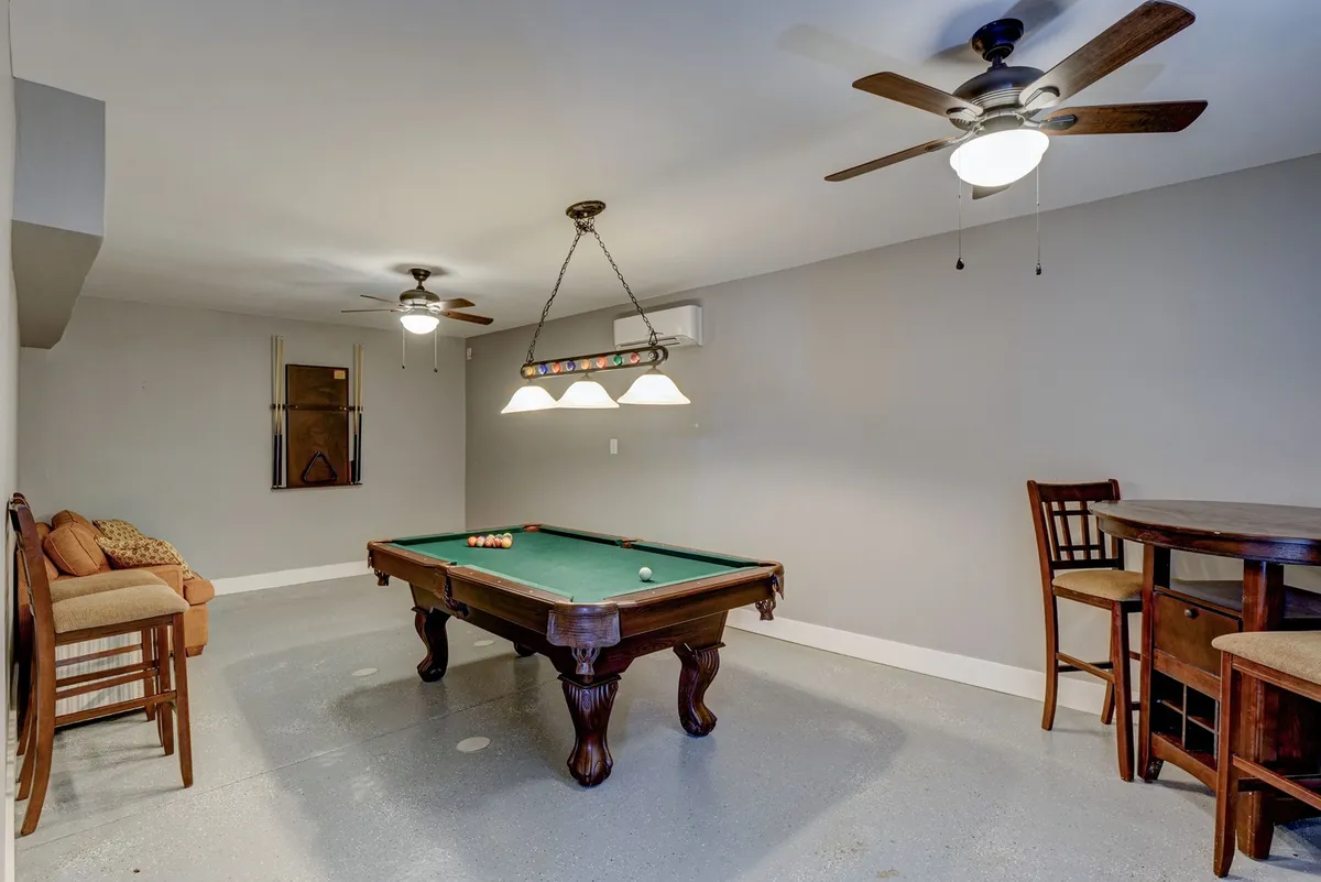 This interior image presents a vibrant game room featuring a pool table as its centerpiece, surrounded by bar stools, a comfortable seating area, and attractive light fixtures overhead. The space feels open and social—ideal for friendly competition and group fun.