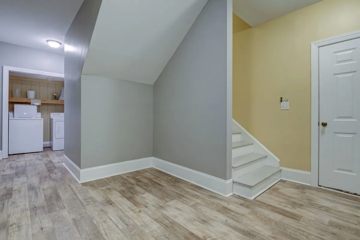 An inviting interior view featuring a staircase, gray and yellow accent walls, and a visible laundry area. The space hints at the transition between living spaces and communal activity areas, setting the stage for family gatherings and indoor fun.