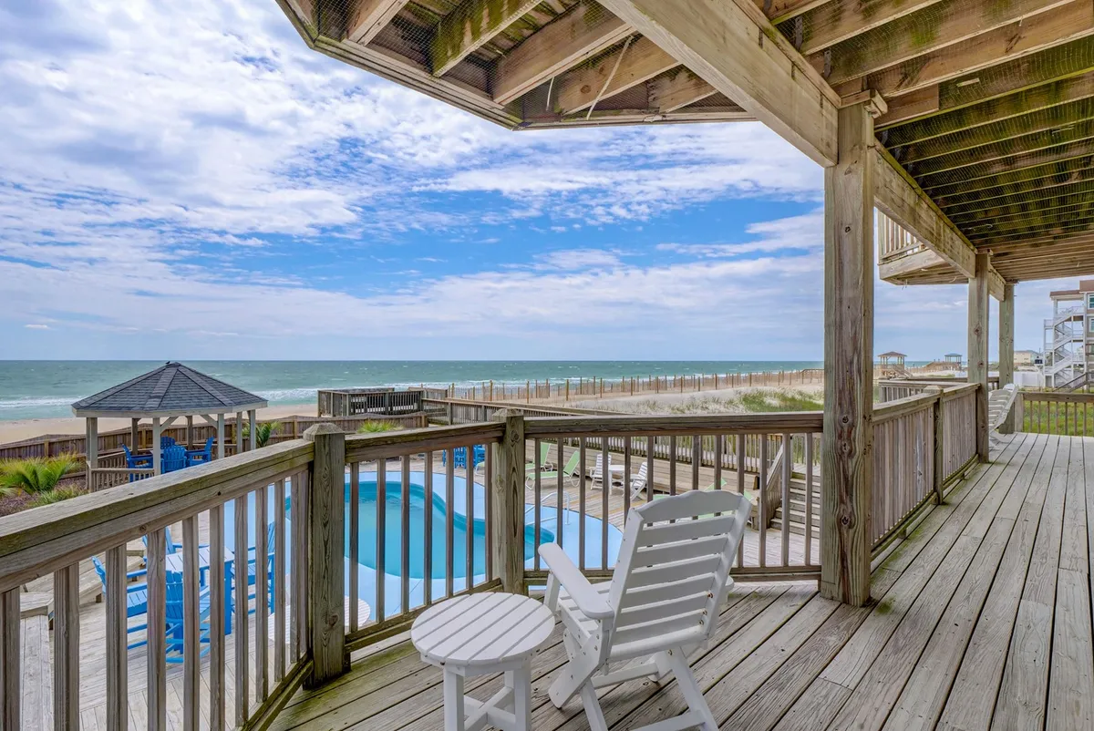A serene poolside setting with a beachfront view, comfortable lounge chairs, a gazebo for shade, and an outdoor seating area. This image captures the tranquil side of poolside living, with clear blue water, spaces for both sunbathing and socializing, and the ocean visible in the background. The scene evokes the luxury of having both pool and beach options at your fingertips.